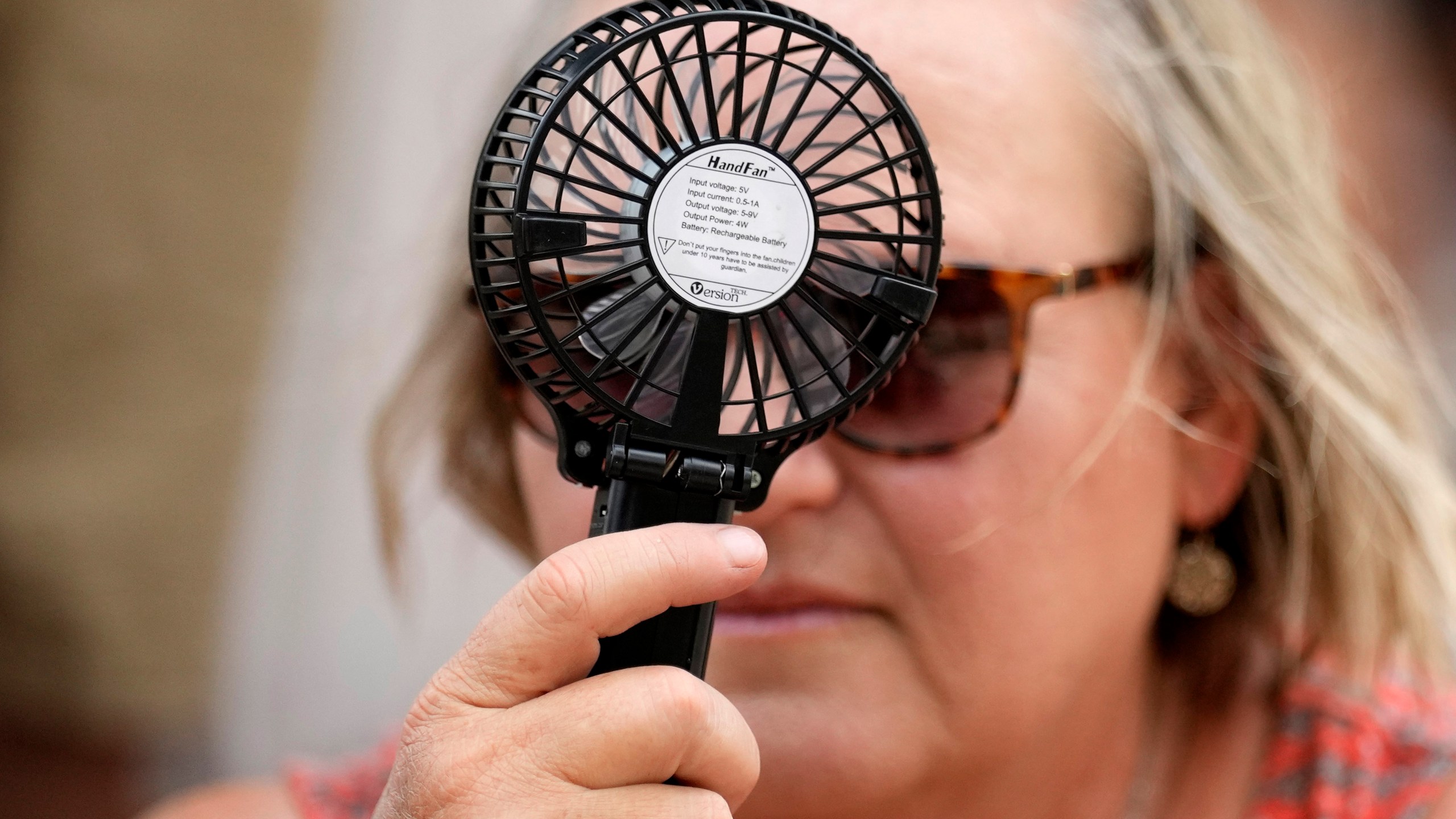 A Houston Astros fan uses a hand fan to keep cool while waiting to enter Minute Maid Park for baseball game against the Cincinnati Reds Saturday, June 17, 2023, in Houston. (AP Photo/David J. Phillip)