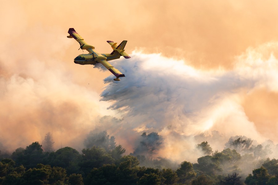 A firefighting plane sprays water to extinguish a wildfire . (AP Photo/Miroslav Lelas)