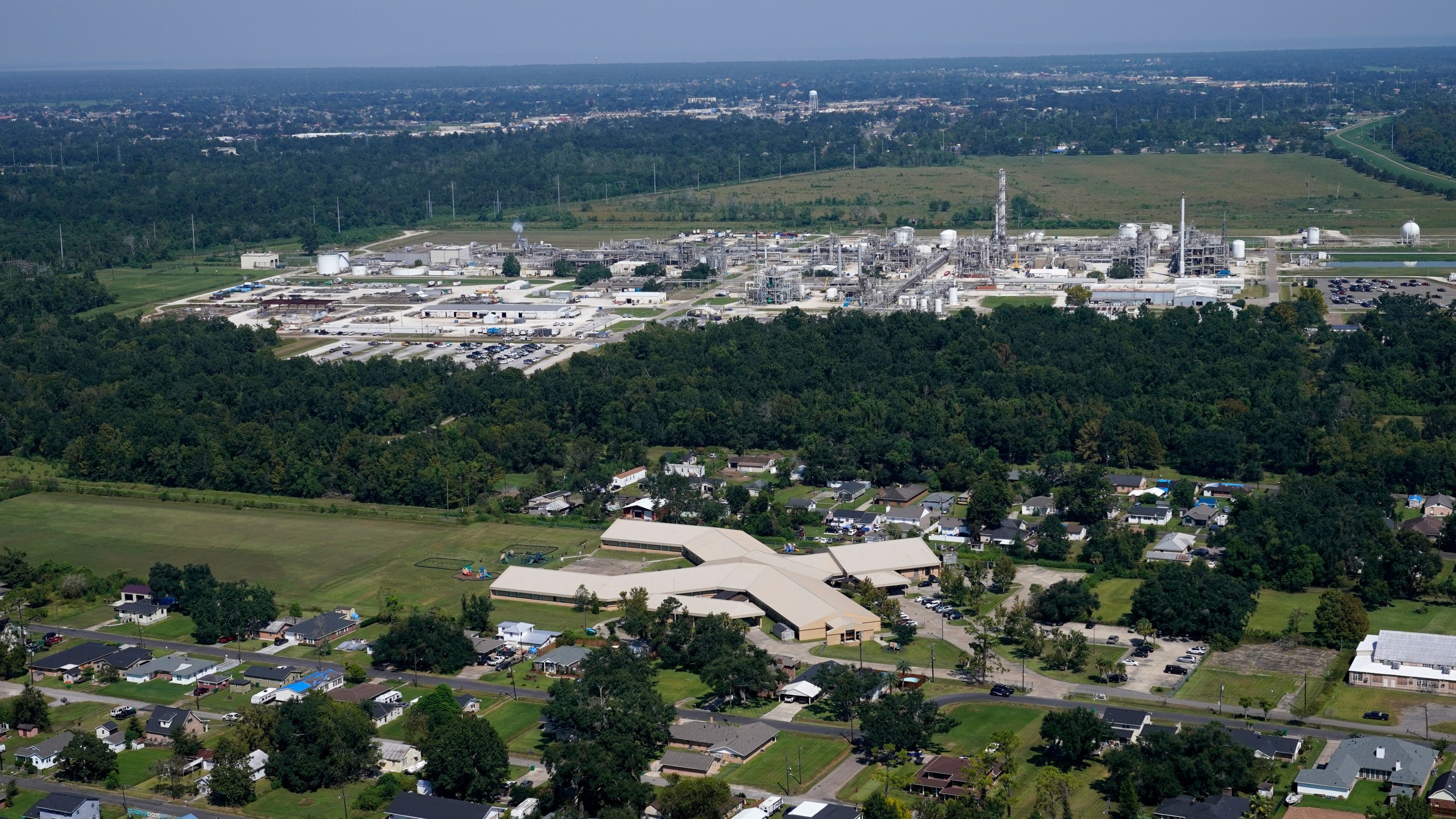 FILE - The Fifth Ward Elementary School and residential neighborhoods sit near the Denka Performance Elastomer Plant, back, in Reserve, La., Friday, Sept. 23, 2022. Denka Performance Elastomer in Louisiana threatened to shut down if the Biden administration doesn’t give it more time to reduce its emissions. The company makes the synthetic rubber neoprene — and federal officials have accused the plant of increasing cancer risk to the nearby, majority-Black community. (AP Photo/Gerald Herbert, File)