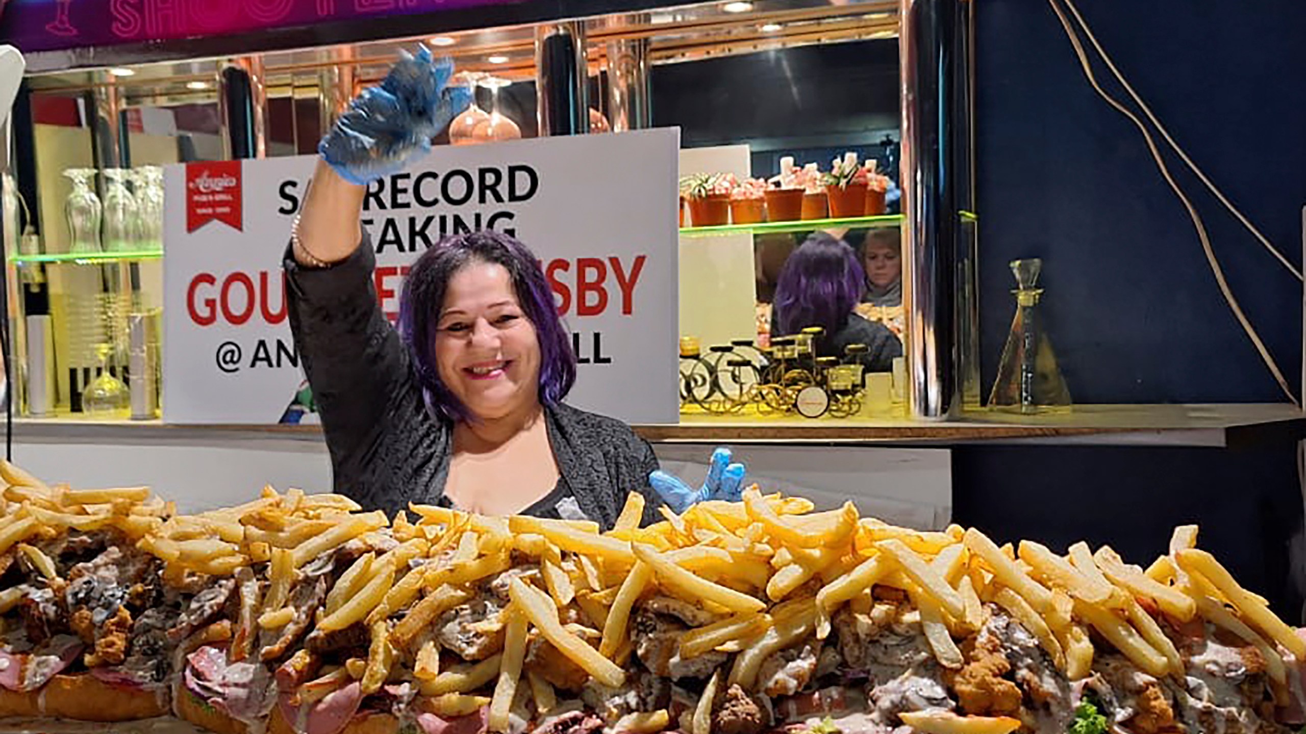 In this photo provided by Joe Redelinghuys. left, for Annies Ladies Bar, Annie Redelinghuys poses with a giant Gatsby sandwich on display at the establishment in Cape Town, South Africa, Saturday, June 29, 2024. A South African restaurant and bar has served up a 3-meter-long (9.8 feet) sandwich in the latest offering from an establishment with a taste for the supersize. (Annies Ladies Bar via AP)