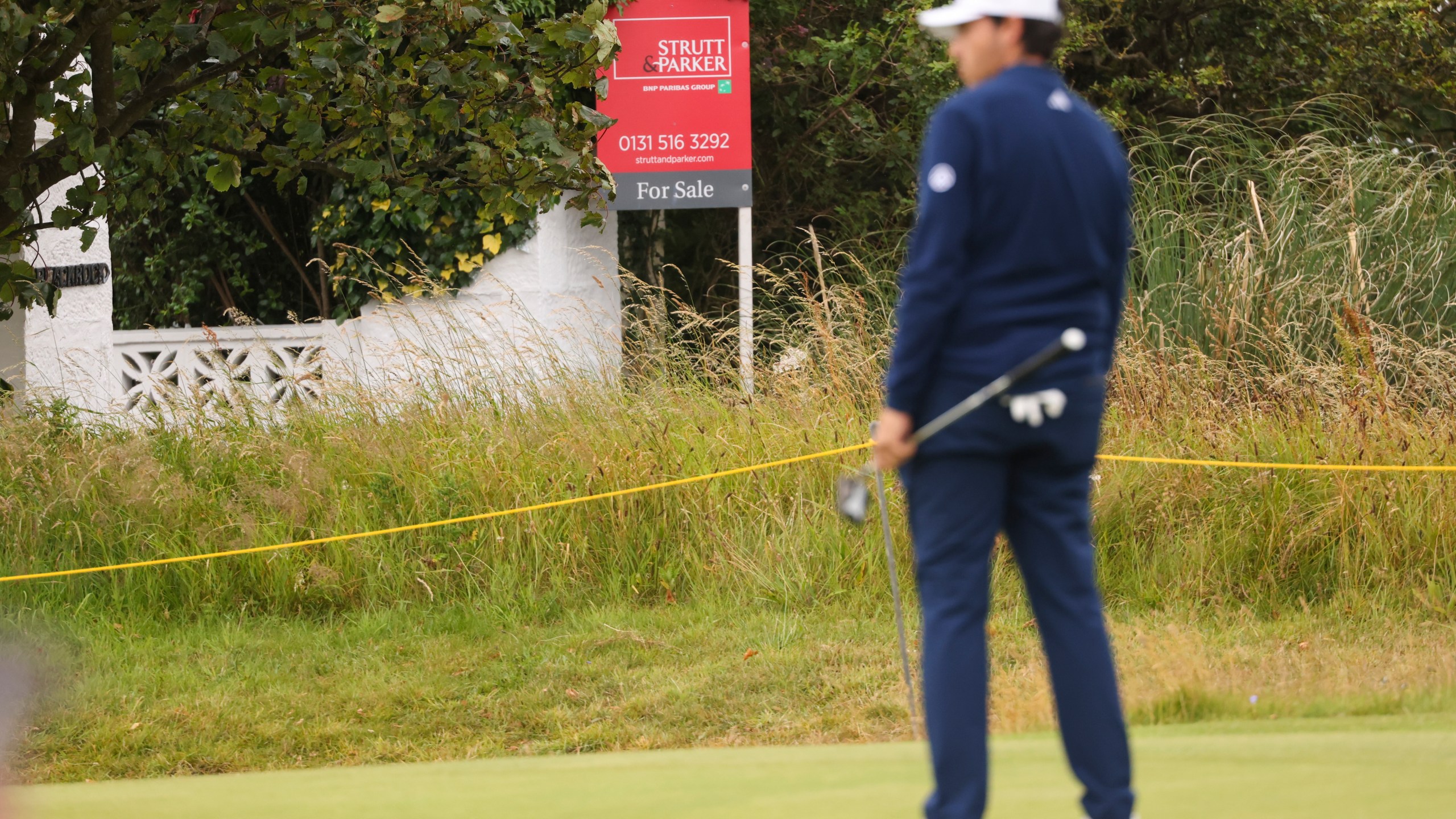 A golfer waits to putt on the 17th green, near "Blackrock house" that is listed for sale near the second and 16th holes at Royal Troon golf club, venue for the British Open Golf Championships, in Troon, Scotland, Tuesday, July 16, 2024. Royal Troon has some unique aspects but maybe most curious is the private house that sits in the middle of the championship course and has views of five holes. (AP Photo/Peter Morrison)