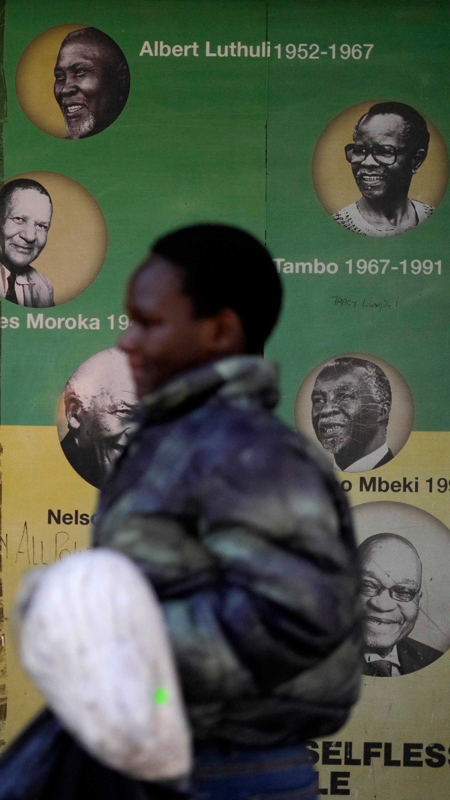 A woman walks past a wallpaper with portraits of the former ruling party presidents outside Luthuli House in downtown Johannesburg, South Africa, Wednesday, July 17, 2024. Former South African President Jacob Zuma was expected to face a disciplinary hearing with the African National Congress party on Wednesday, after campaigning against the organization he once led as head of a new political party in national elections in May. (AP Photo/Themba Hadebe)