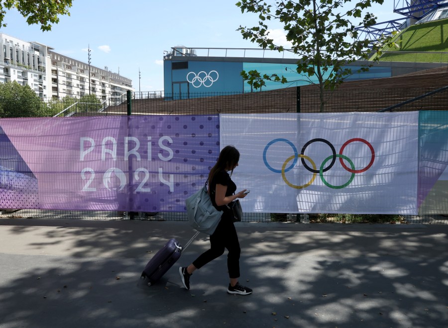 A woman pulls her luggage by Paris 2024 Olympic banners, just nine days before the start of the Paris Olympic games, Wednesday, July 17, 2024 in Paris. (AP Photo/Aurelien Morissard)