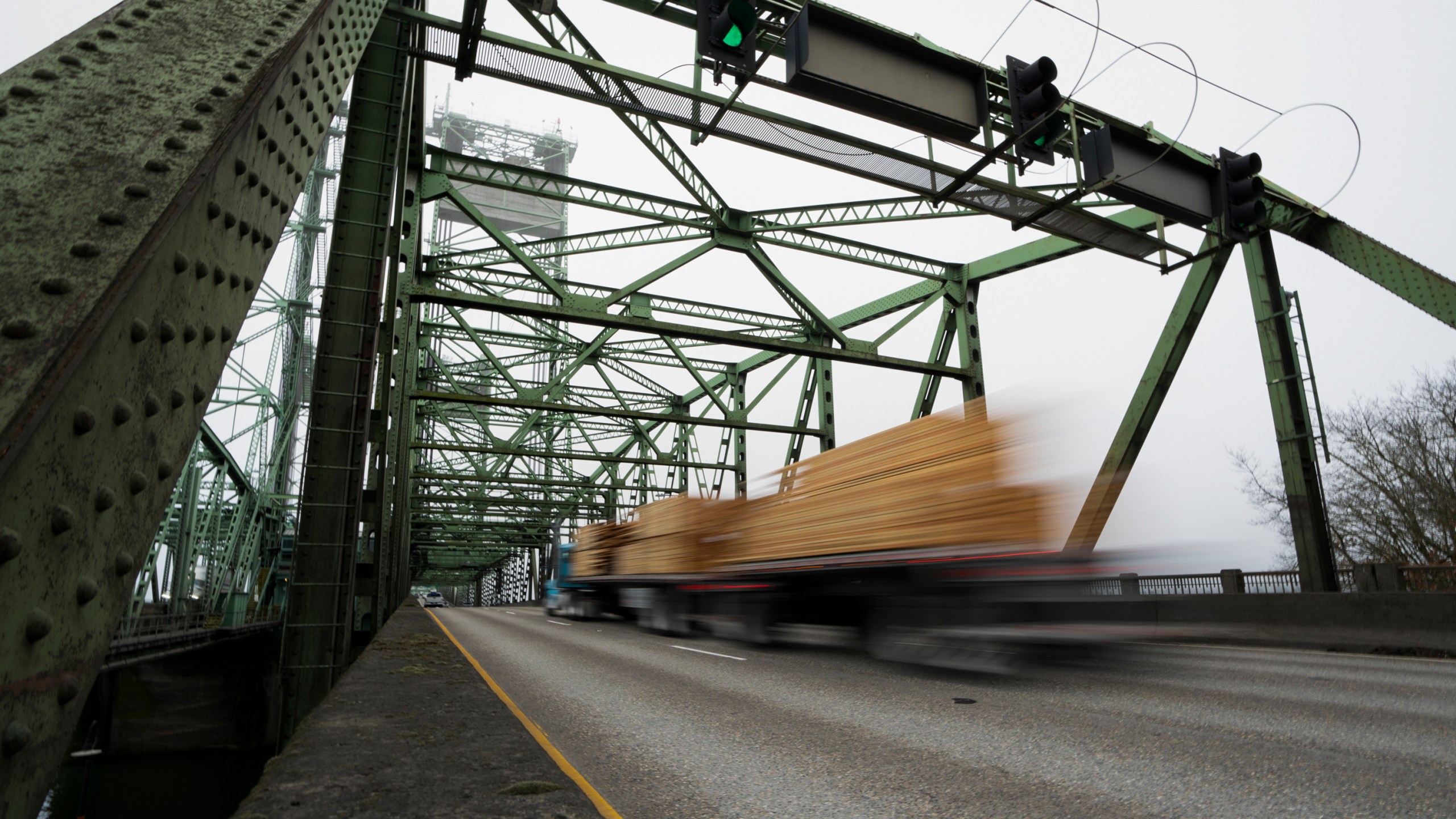 FILE - A logging truck drives on the Interstate 5 bridge that spans the Columbia River and connects Portland, Ore., with southwest Washington state, Feb. 13, 2024. Dozens of aging bridges, including this Interstate 5 bridge, in 16 states will be replaced or improved with the aid $5 billion of federal grants announced Wednesday, July 17, by President Joe Biden's administration as the latest beneficiaries of a massive infrastructure law. (AP Photo/Jenny Kane, File)