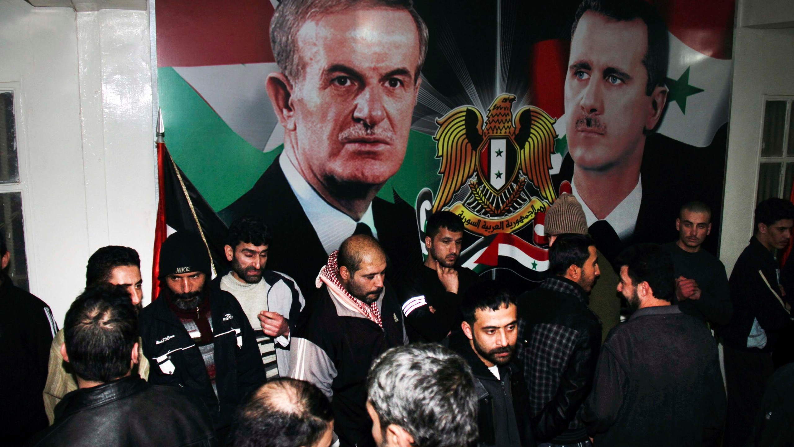 FILE - Freed Syrian detainees gather in front of posters showing Syrian President Bashar Assad, right, and his father Hafez Assad after they were released from Adra Prison on the north-east outskirts of Damascus, Syria, on Jan. 15, 2013. A former Syrian military official who oversaw the prison where human rights officials say torture and abuse took place has been arrested in Los Angeles on suspicion of immigration fraud. (AP Photo/Bassem Tellawi, File)