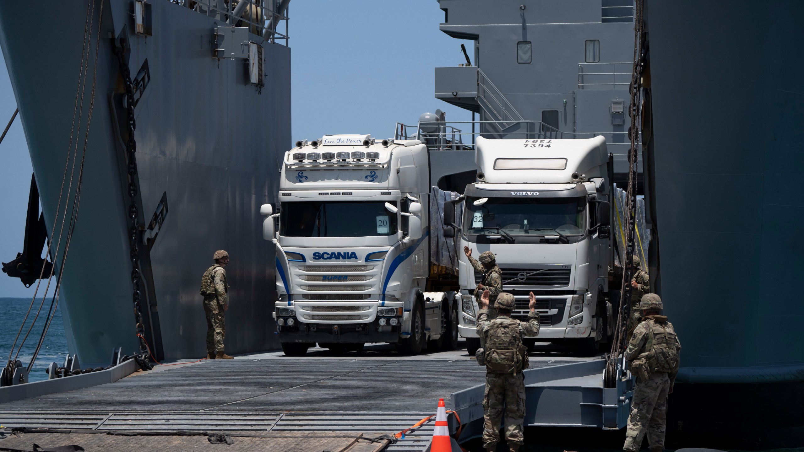 U.S. Army soldiers gestures as trucks loaded with humanitarian aid arrive at the U.S.-built floating pier Trident before reaching the beach on the coast of the Gaza Strip, Tuesday, June 25, 2024. (AP Photo/Leo Correa)